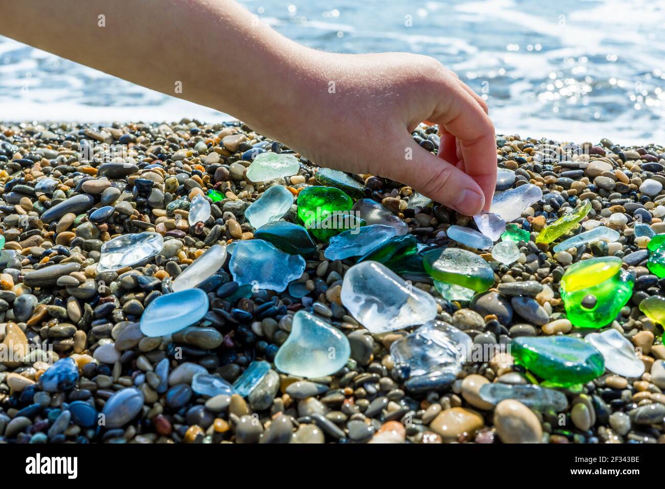 Morceaux de verre de mer polis et colorés recueillis de la plage dans une  main d'enfant. Beau gros plan de verre vert, bleu et blanc sur une plage de  mer de retour
