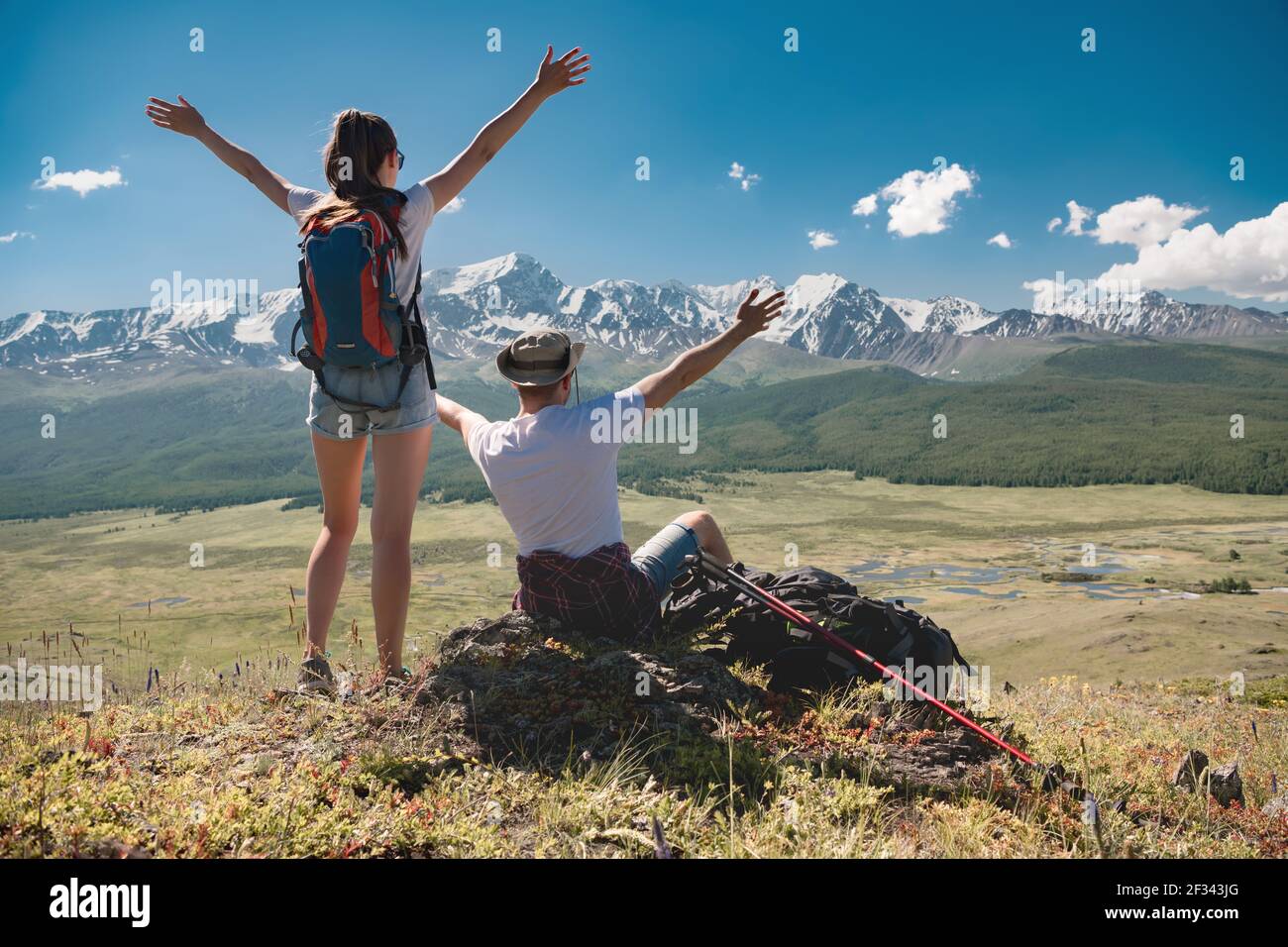 Un couple heureux de jeunes randonneurs se tient debout avec les bras levés sur fond de montagnes enneigées Banque D'Images
