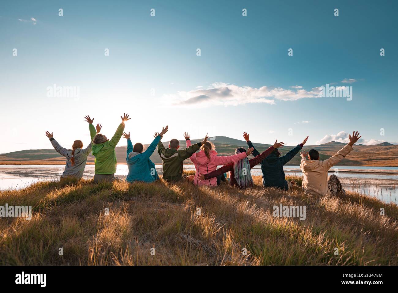 Grand groupe de touristes heureux sont assis avec les bras levés au beau coucher de soleil lac et montagnes Banque D'Images