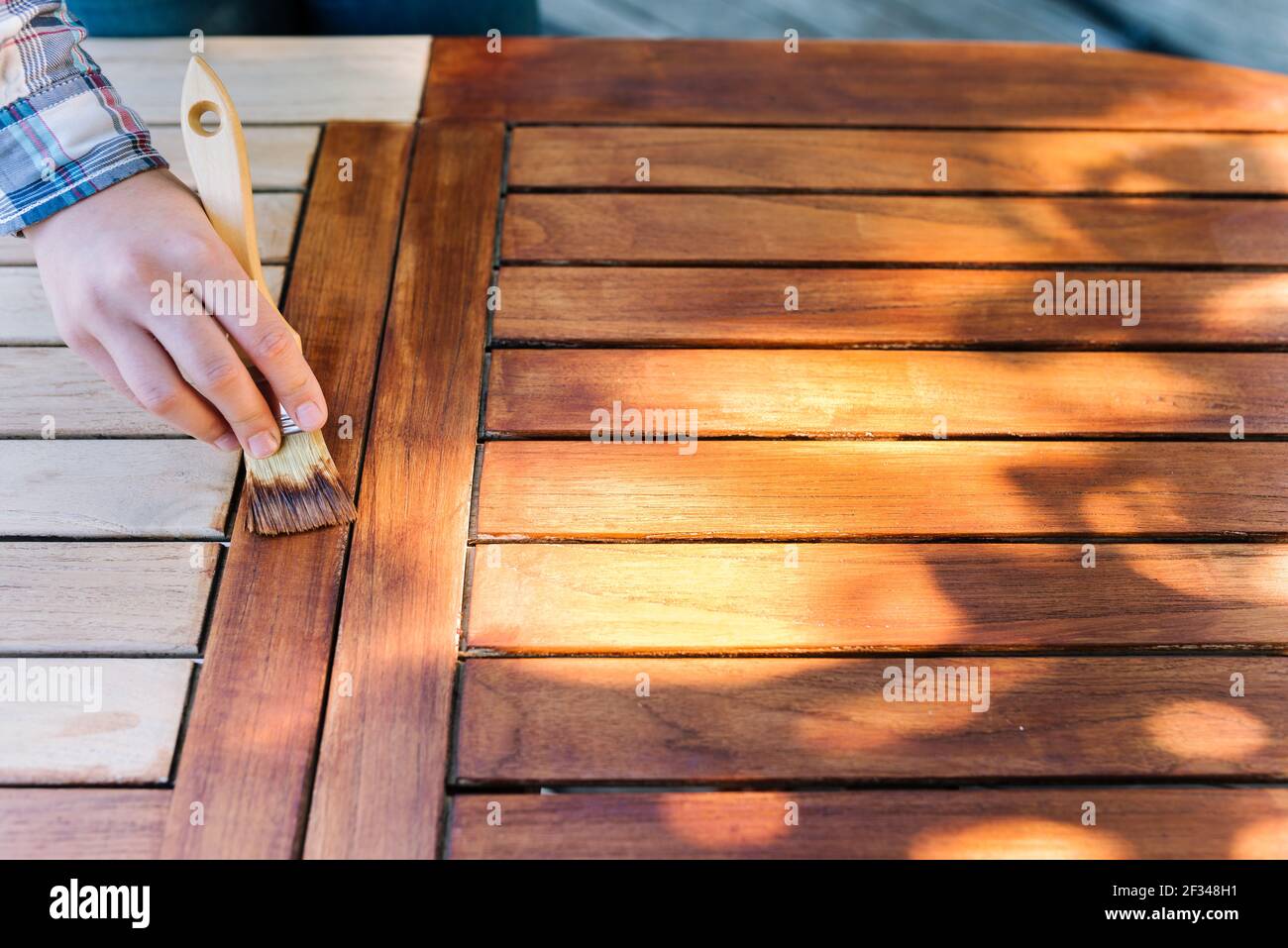 main femelle tenant un pinceau appliquant de la peinture vernis sur un table de jardin en bois - peinture et entretien du bois avec huile Banque D'Images