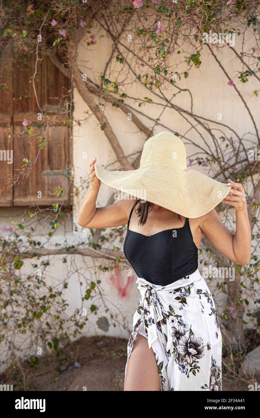 Une jeune femme se cache du soleil sous un grand chapeau de paille près  d'un mur enturé de branches sèches d'un arbre en fleur Photo Stock - Alamy