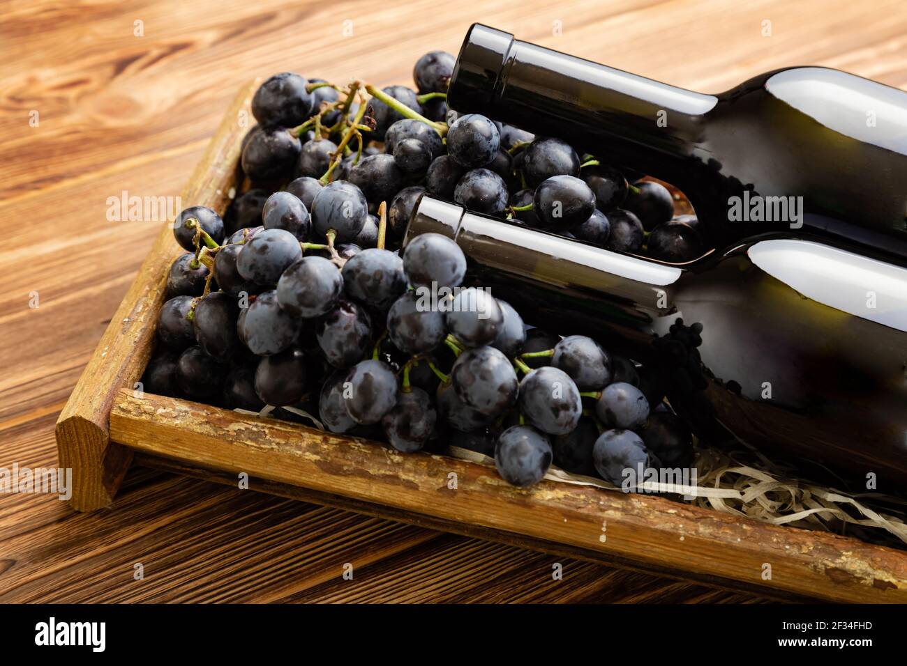 Composition de deux bouteilles de vin rouge sur une table en bois brun. Bouteilles de vin rouge en boîte sur des raisins mûrs noirs sur une table en bois. Vin de collection ancien Banque D'Images