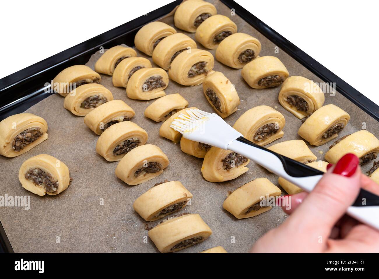 Une femme applique de l'huile sur des gâteaux de levure fraîchement faits, crus avec des champignons à l'intérieur à l'aide d'une truelle de cuisson en silicone. Banque D'Images