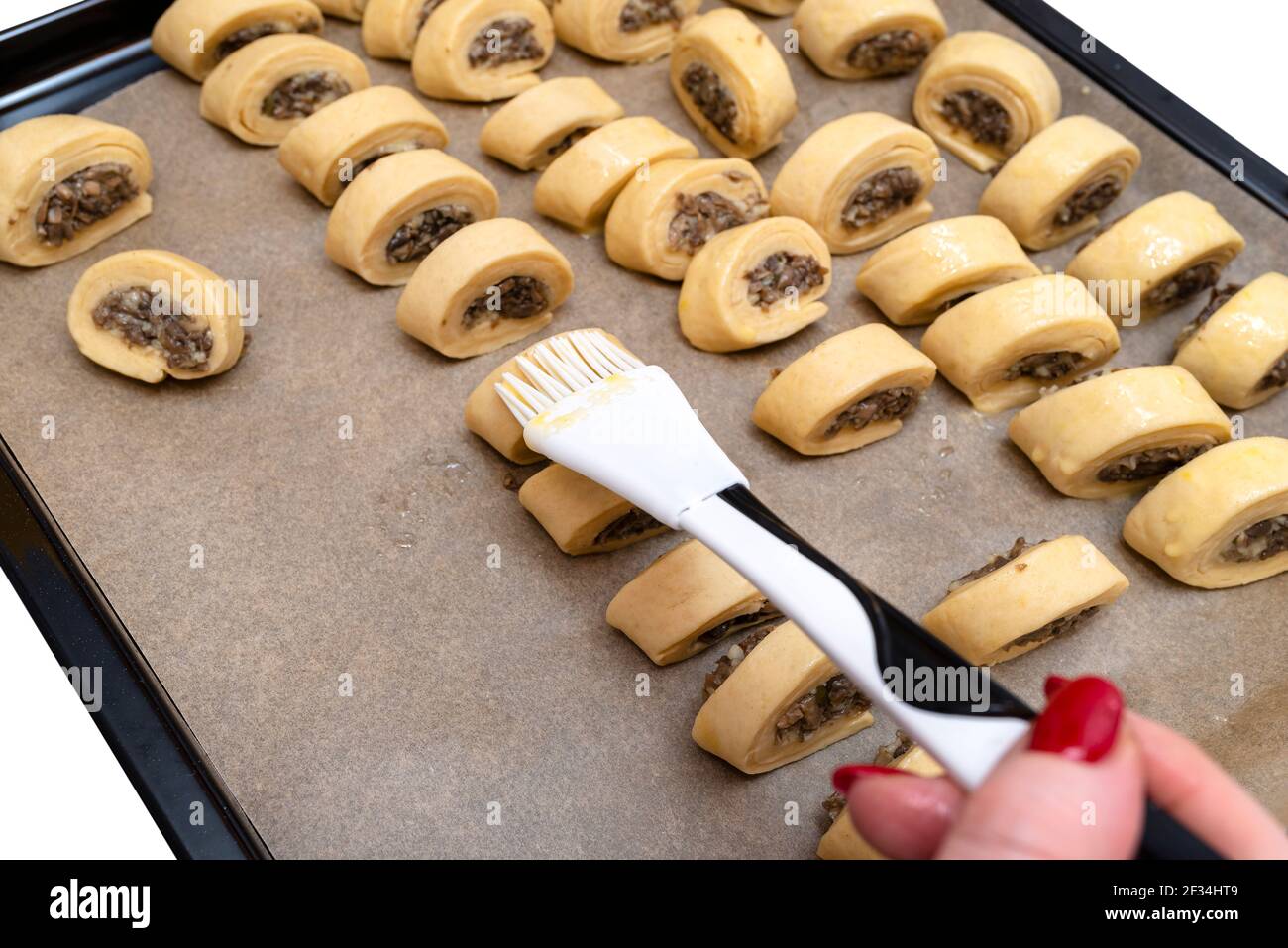 Une femme applique de l'huile sur des gâteaux de levure fraîchement faits, crus avec des champignons à l'intérieur à l'aide d'une truelle de cuisson en silicone. Banque D'Images