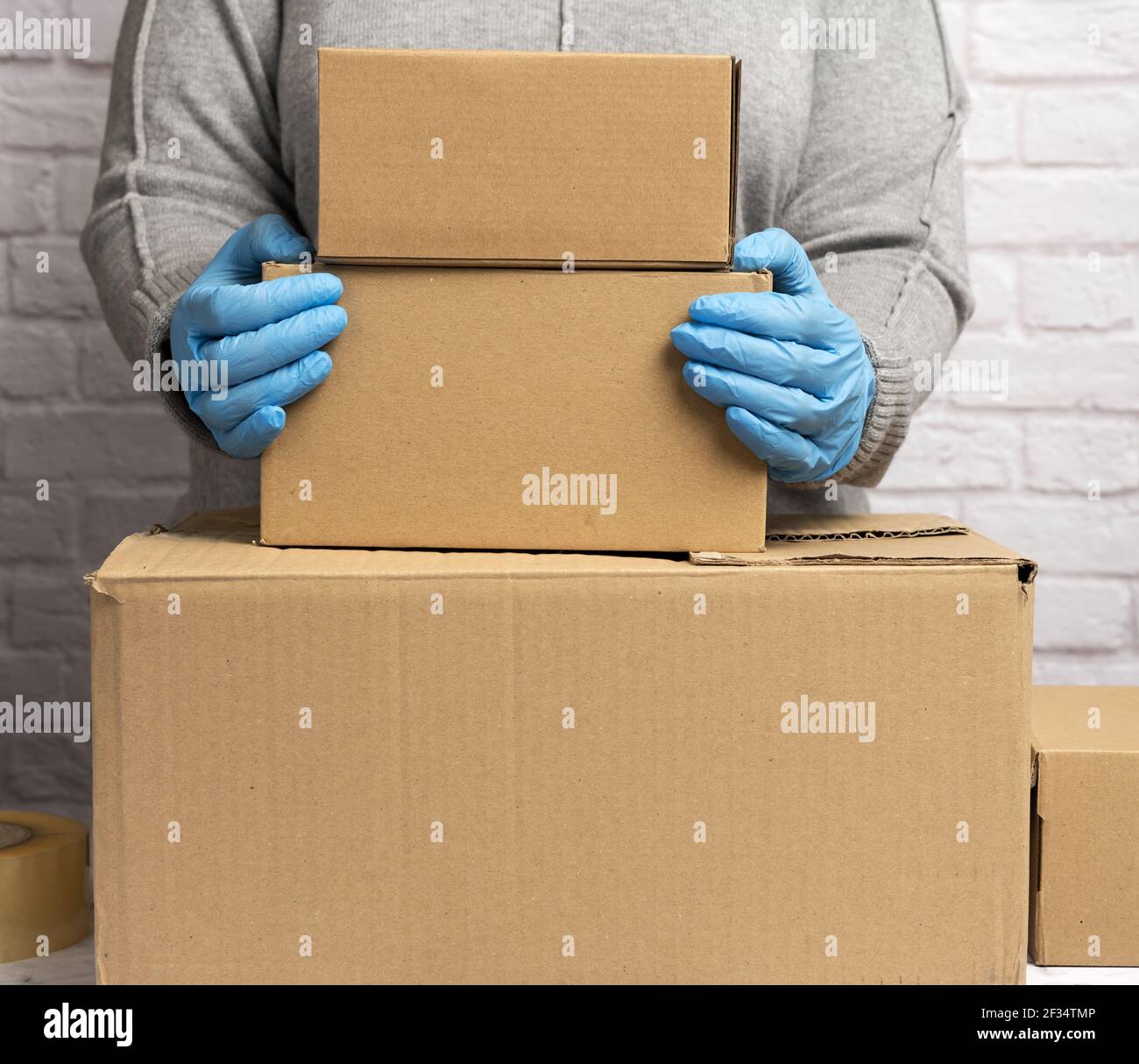 une femme dans un chandail gris est emballage et des gants bleus tient une pile de cartons bruns, en mouvement, don Banque D'Images