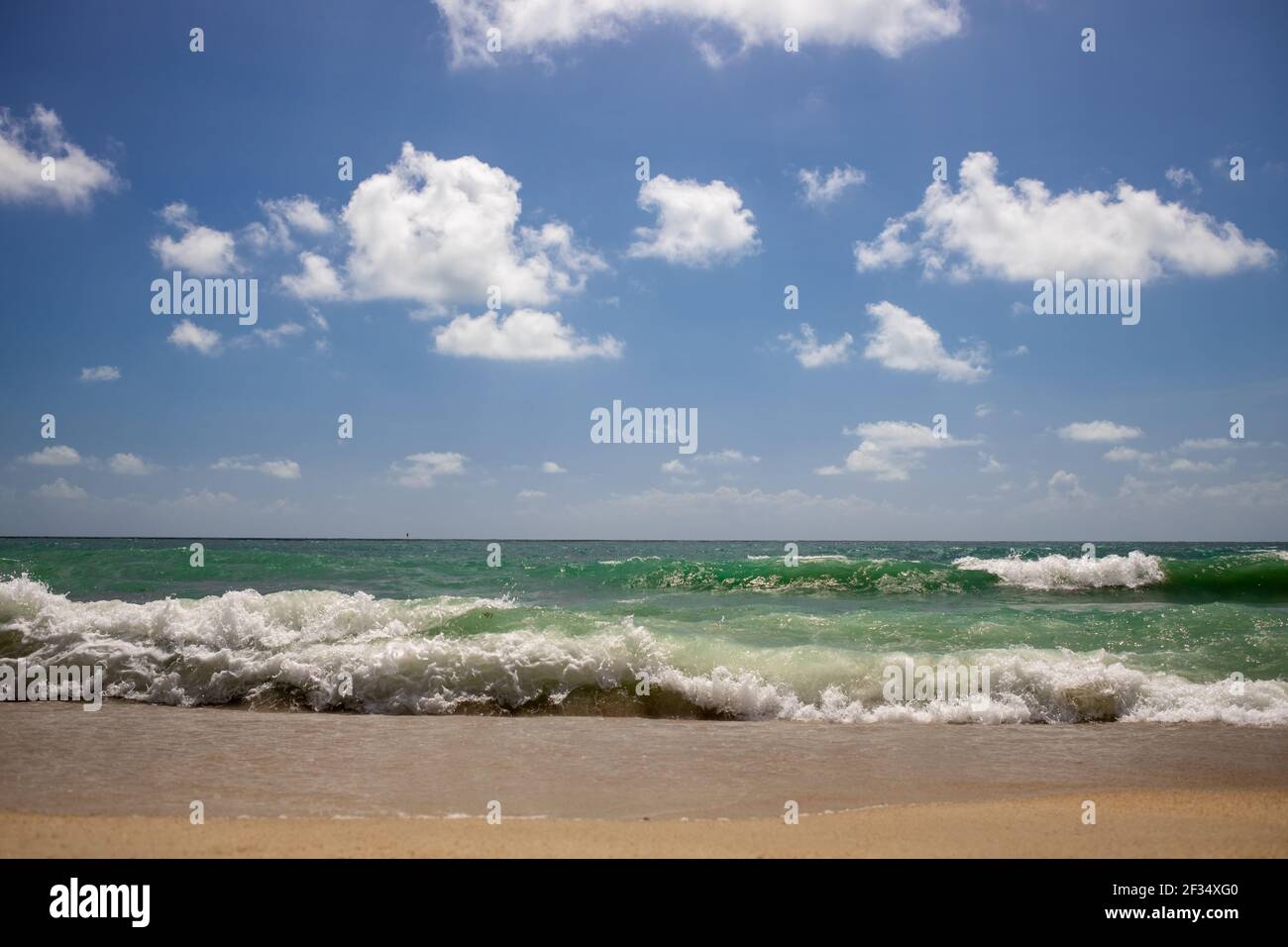 de fortes vagues sur une belle plage de sable avec un ciel bleu nuageux. Banque D'Images