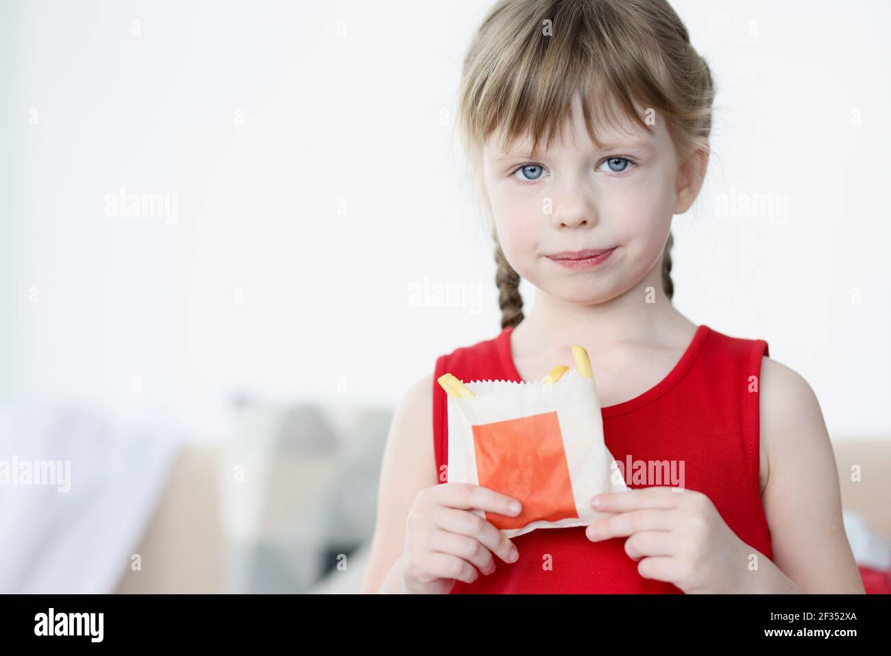 La petite fille tient les frites dans son emballage dans ses mains Banque D'Images