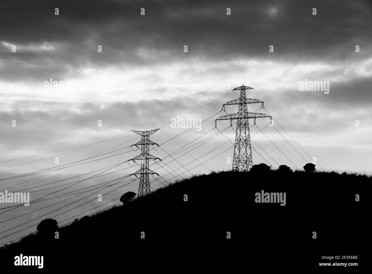 Silhouette de tours électriques sur un sommet d'une colline.contre un ciel spectaculaire avec des nuages. Banque D'Images