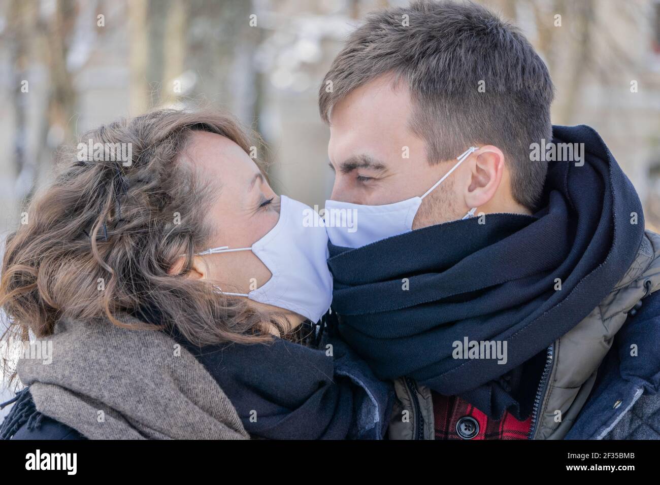 Couple embrassant portant des masques de visage à l'extérieur. L'homme et la femme baiser à travers les masques faciaux à l'extérieur. Couple charmant dans les masques médicaux de protection regardant chacun Banque D'Images