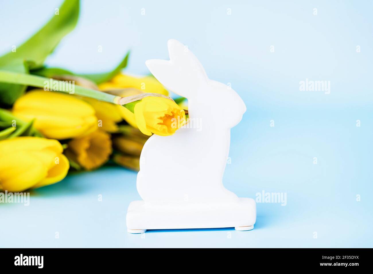 Lapin de Pâques en céramique blanche, jonquilles jaunes et tulipes sur fond bleu Banque D'Images