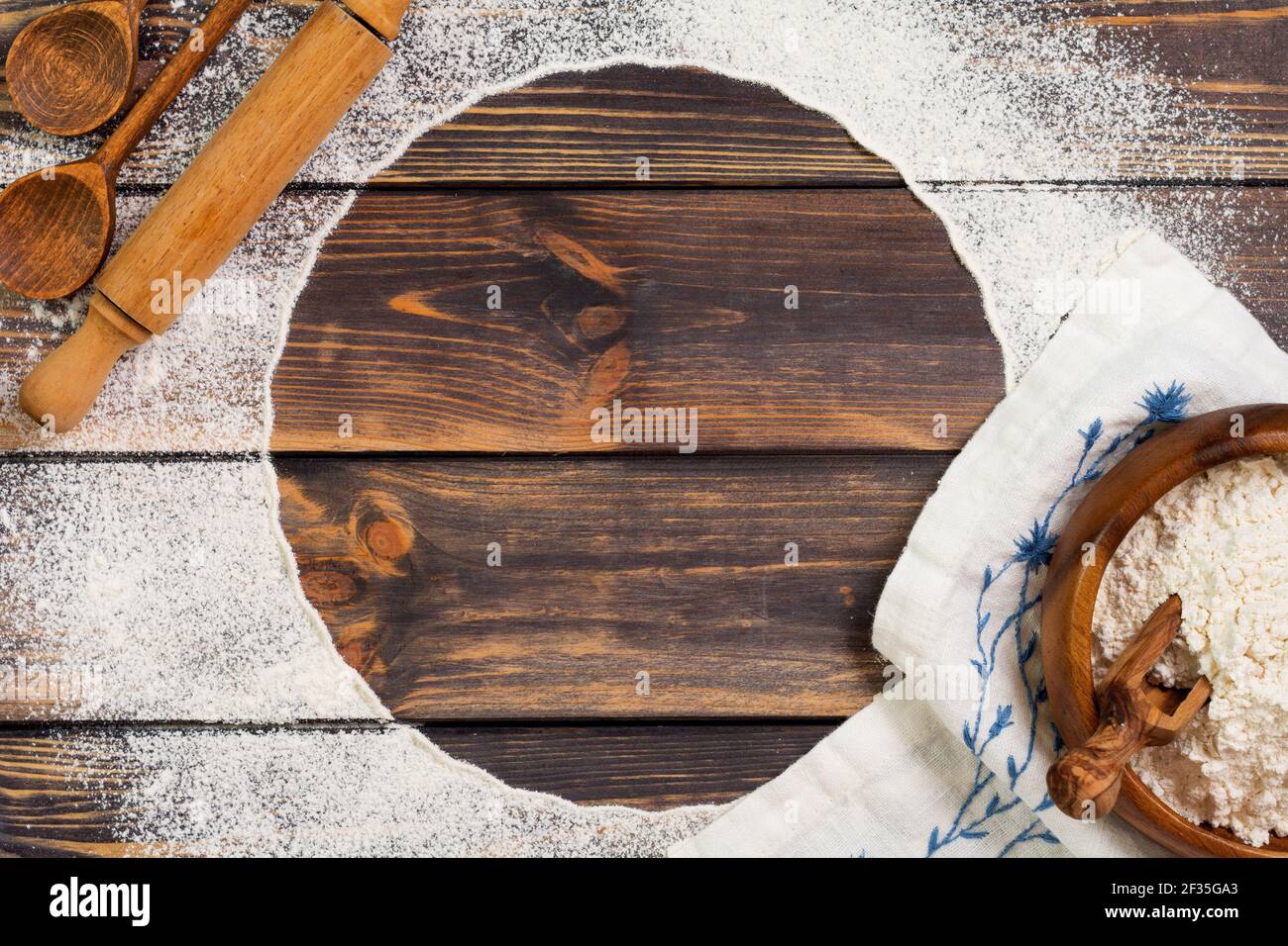 Farine dispersée sous la forme d'un cercle, d'une broche roulante et d'une serviette en lin blanc sur un vieux fond en bois. Placer pour le texte. Fond pour la cuisson. Banque D'Images