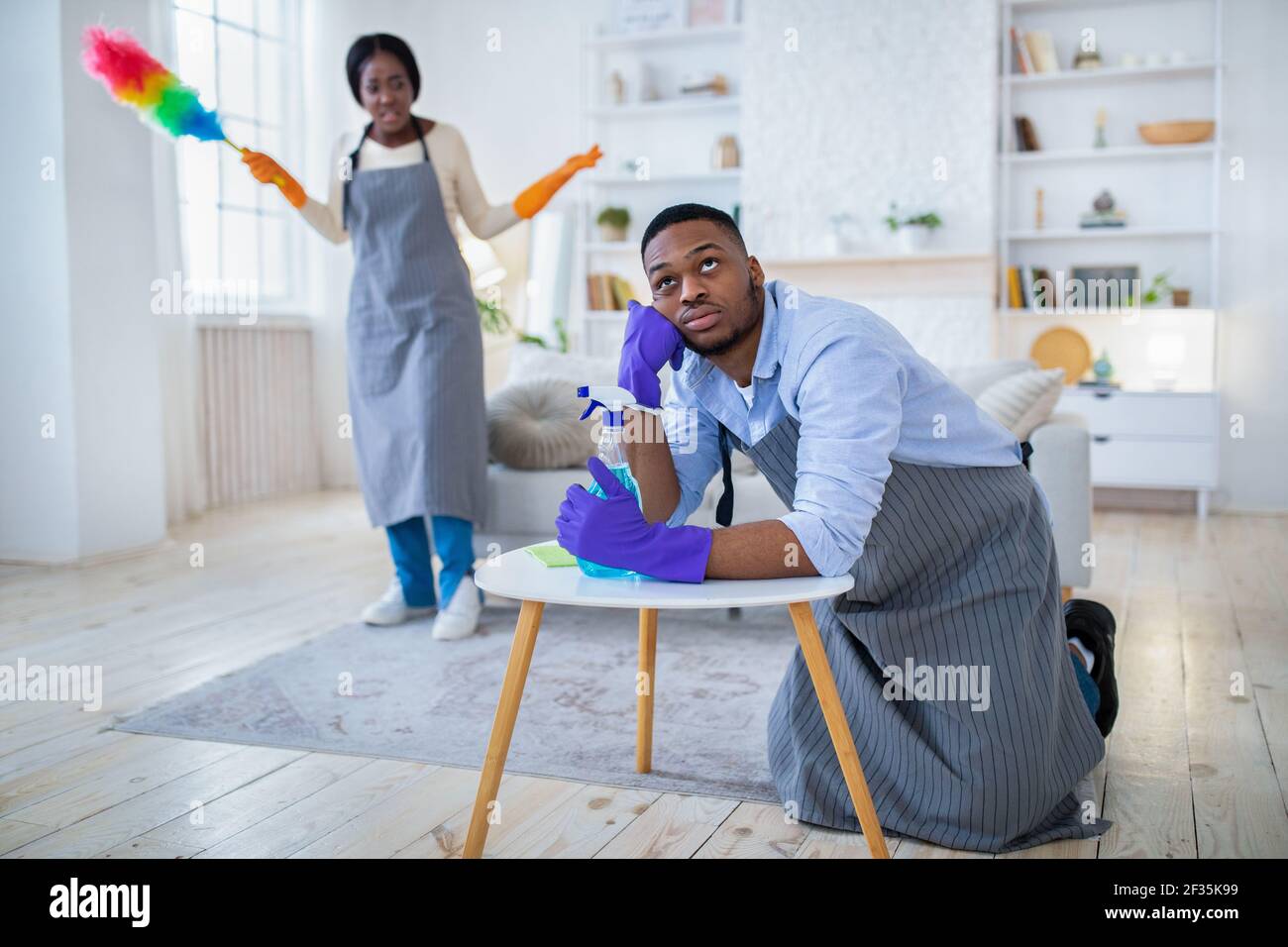 Jeune homme noir fatigué des travaux ménagers, sa femme en colère le colant pour ne rien faire, copier l'espace Banque D'Images