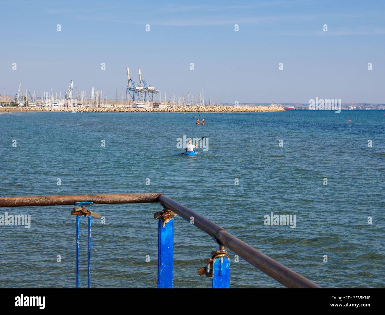 Vue depuis la jetée sur l'homme pagayant en canoë et les personnes nageant dans la mer méditerranée à Larnaca, Chypre. Banque D'Images