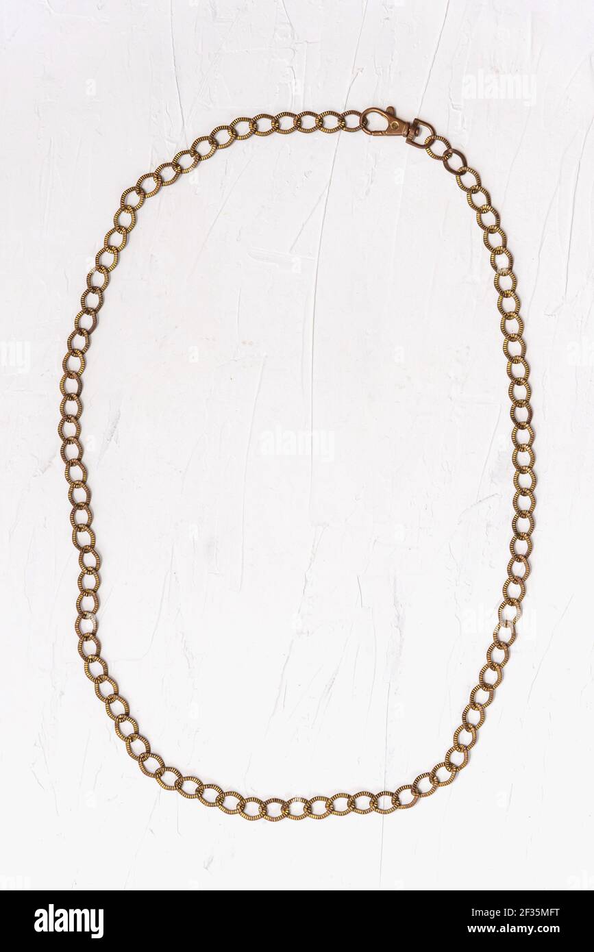 Accessoire rétro tendance en métal doré chaîne de ceinture fermée par un fermoir placé dans un cadre ovale vertical sur un arrière-plan blanc Banque D'Images