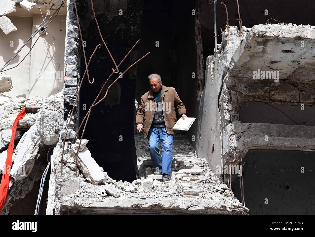 Homs, ville de Homs dans le centre de la Syrie. 11 mars 2021. Hadi Ghusoun, professeur d'anglais à la retraite à la fin des années 60, descend les escaliers de sa maison brisée dans la ville de Homs, dans le centre de la Syrie, le 11 mars 2021. POUR ALLER AVEC: 'Feature: Après 10 ans de guerre syrienne, les personnes âgées abandonnent l'espoir de retourner à la maison' crédit: Ammar Safarjalani/Xinhua/Alay Live News Banque D'Images