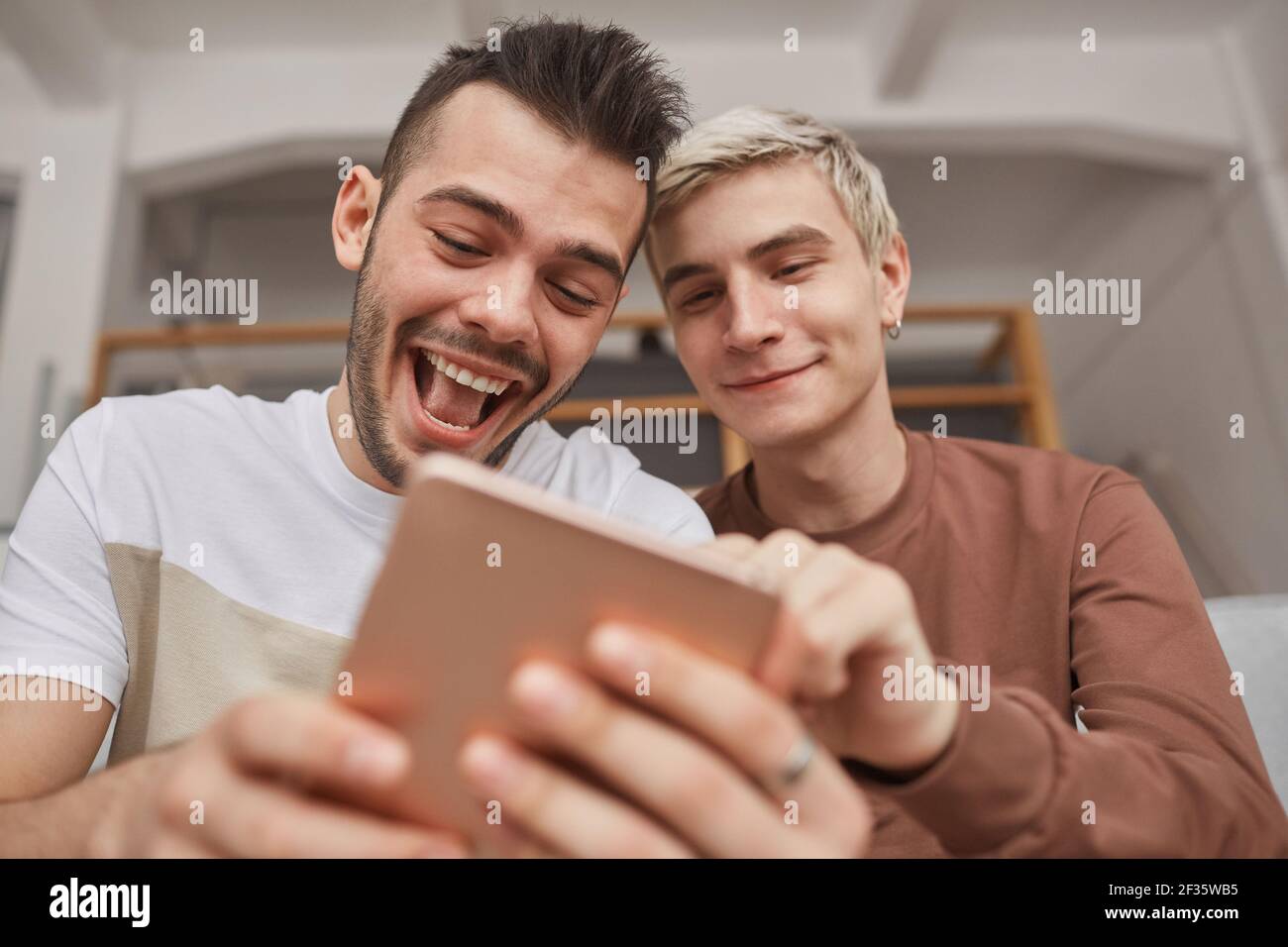 Portrait à angle bas de deux jeunes hommes qui rient en regardant à l'écran de la tablette dans l'intérieur de la maison Banque D'Images