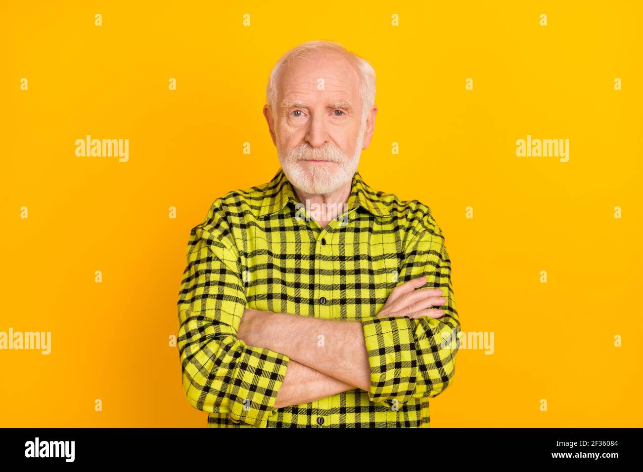 Photo d'un vieil homme sérieux et mûr, mains croisées, aspect grincheux appareil photo porter un tissu écossais vert chemise isolé couleur jaune arrière-plan Banque D'Images