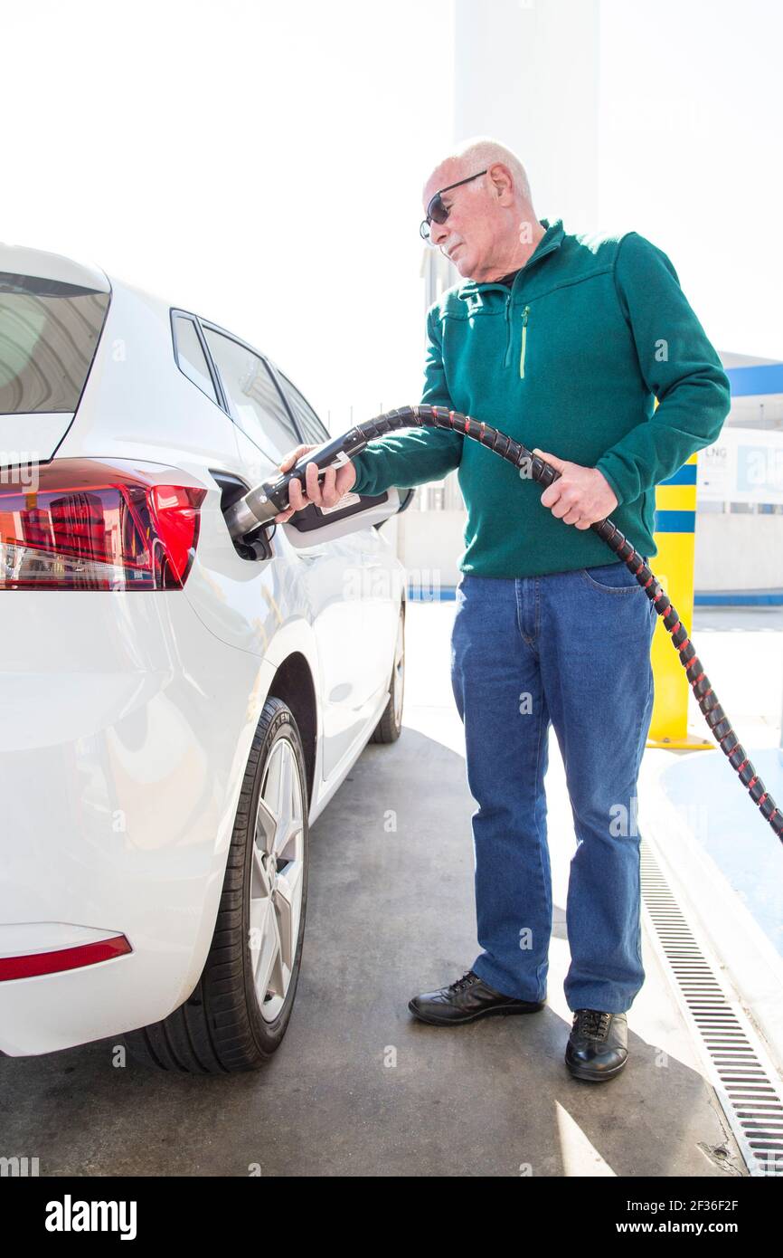 Homme plus âgé avec un chandail vert se remplissant de gnc (gaz naturel comprimé) dans sa voiture écologique. Concept d'énergie propre. Banque D'Images