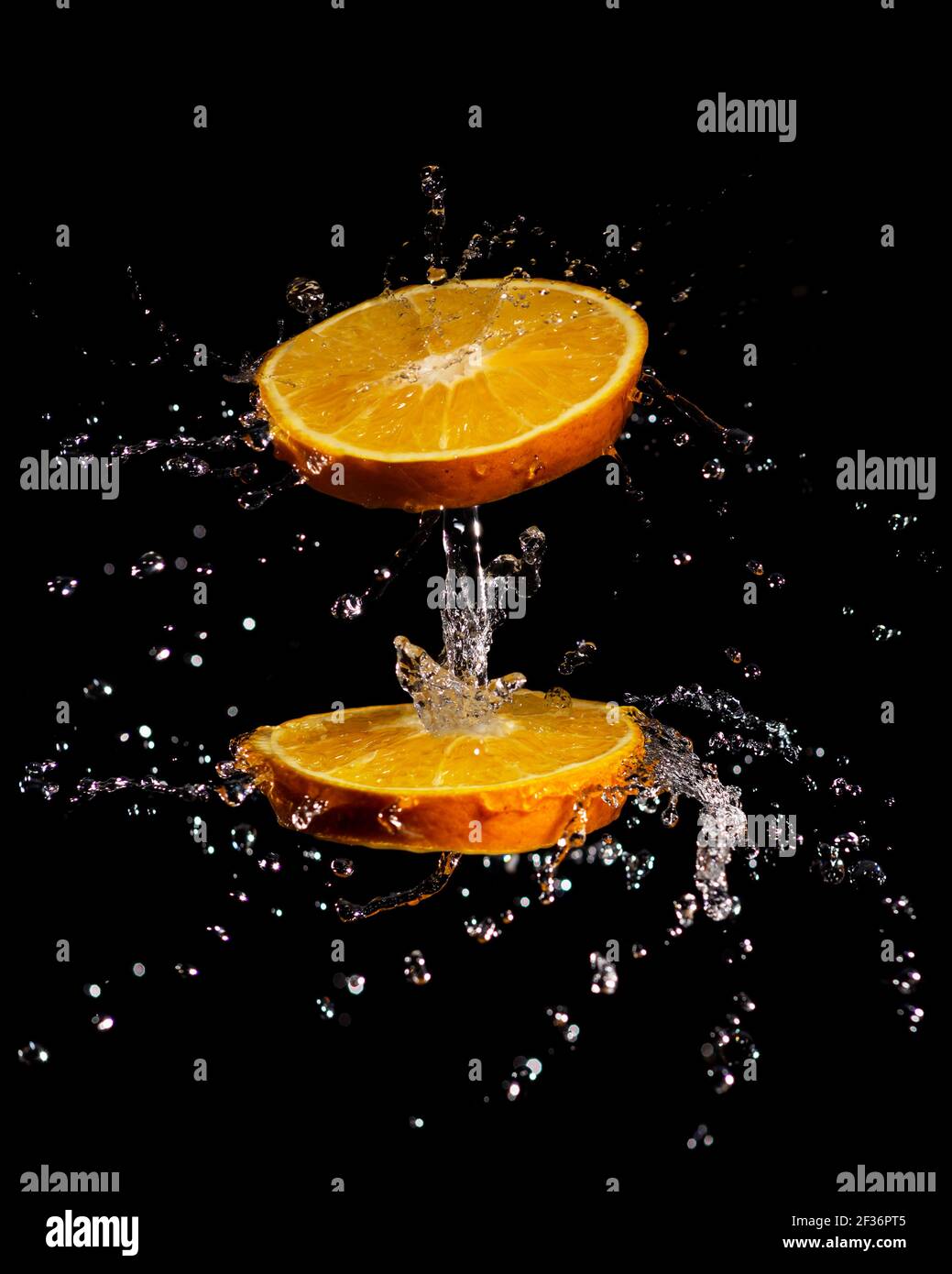 image de composition créative de tranches d'orange juteuses qui tournent et éclabousse eau isolée sur fond noir Banque D'Images