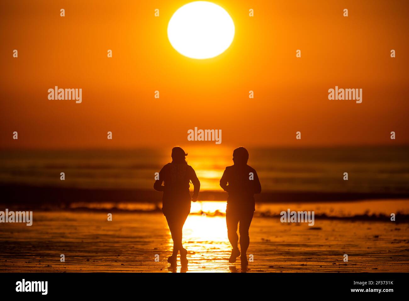 Des membres du public qui s'exécutent le long de la plage à marée basse au lever du soleil à Rustington, dans l'ouest du Sussex Banque D'Images