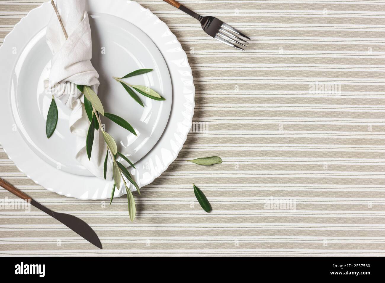 Table festive avec assiette blanche, couverts et décoration avec branches d'olive. Beau plan de pose. Banque D'Images