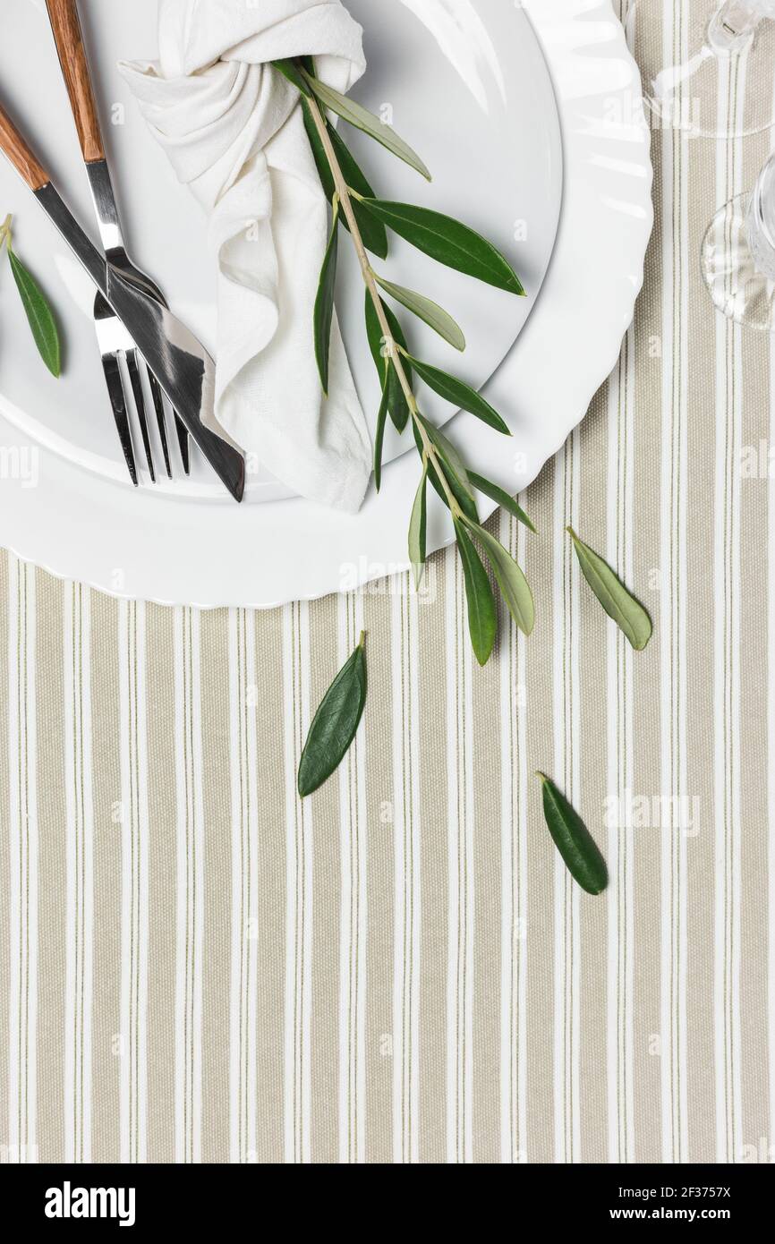 Table festive avec assiette blanche, couverts et décoration avec branches d'olive. Beau plan de pose. Banque D'Images