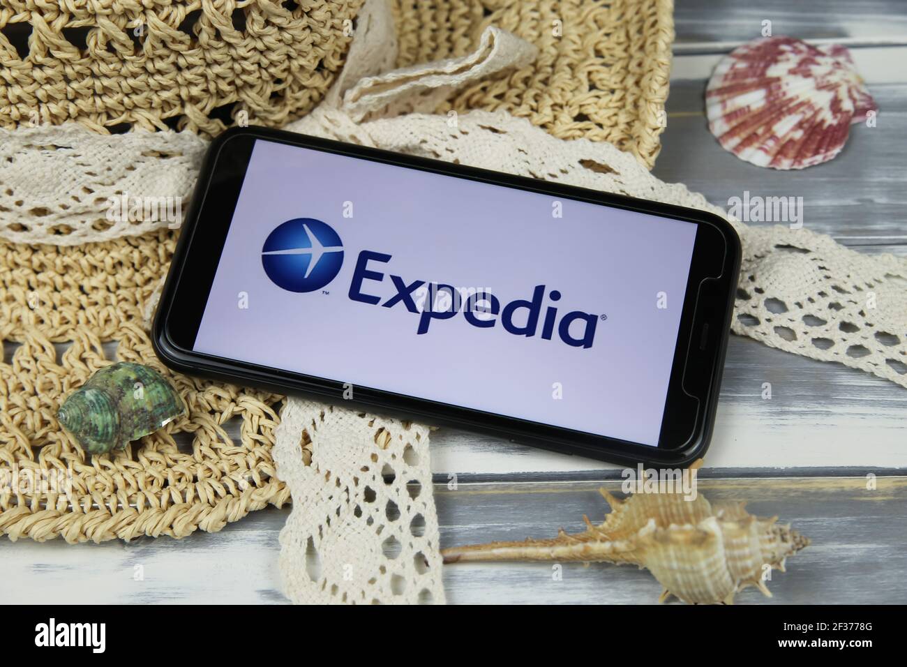 Viersen, Allemagne - 1er mars. 2021: Gros plan de smartphone avec logo de l'agence de voyage Expedia avec chapeau de soleil et coques sur table en bois Banque D'Images