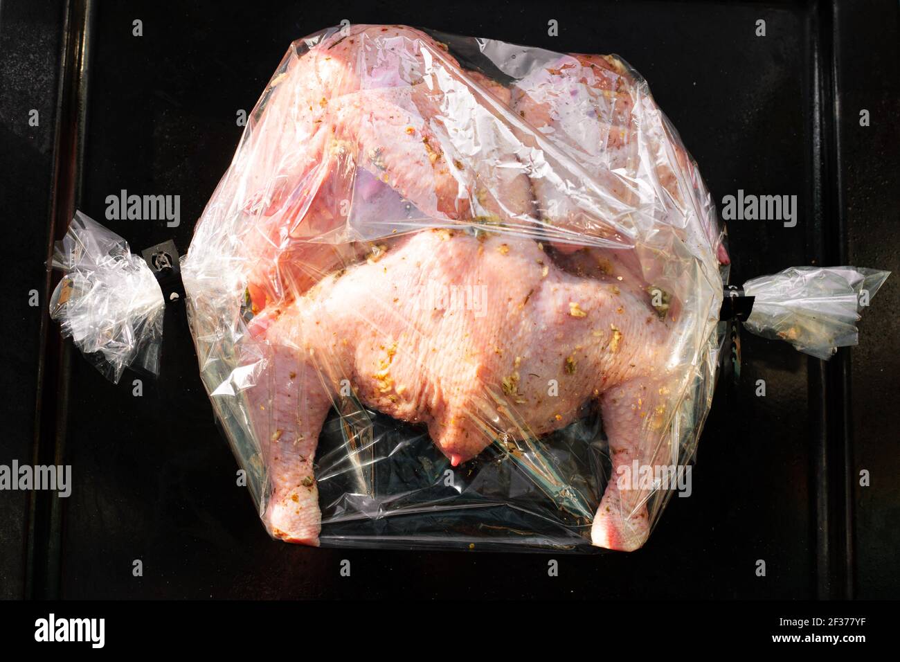 la carcasse de poulet coupée dans le sens de la longueur, marinée dans des  épices, emballable dans un sac en plastique pour cuire au four, repose sur  une plaque de cuisson noire