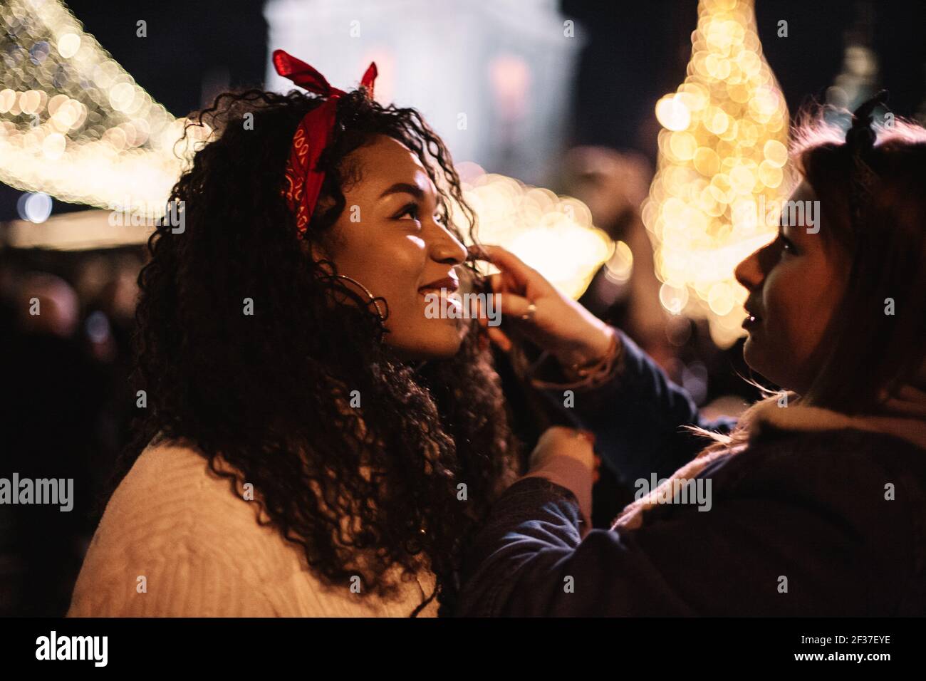 Heureuse jeune femme debout avec petite amie en ville pendant noël Banque D'Images