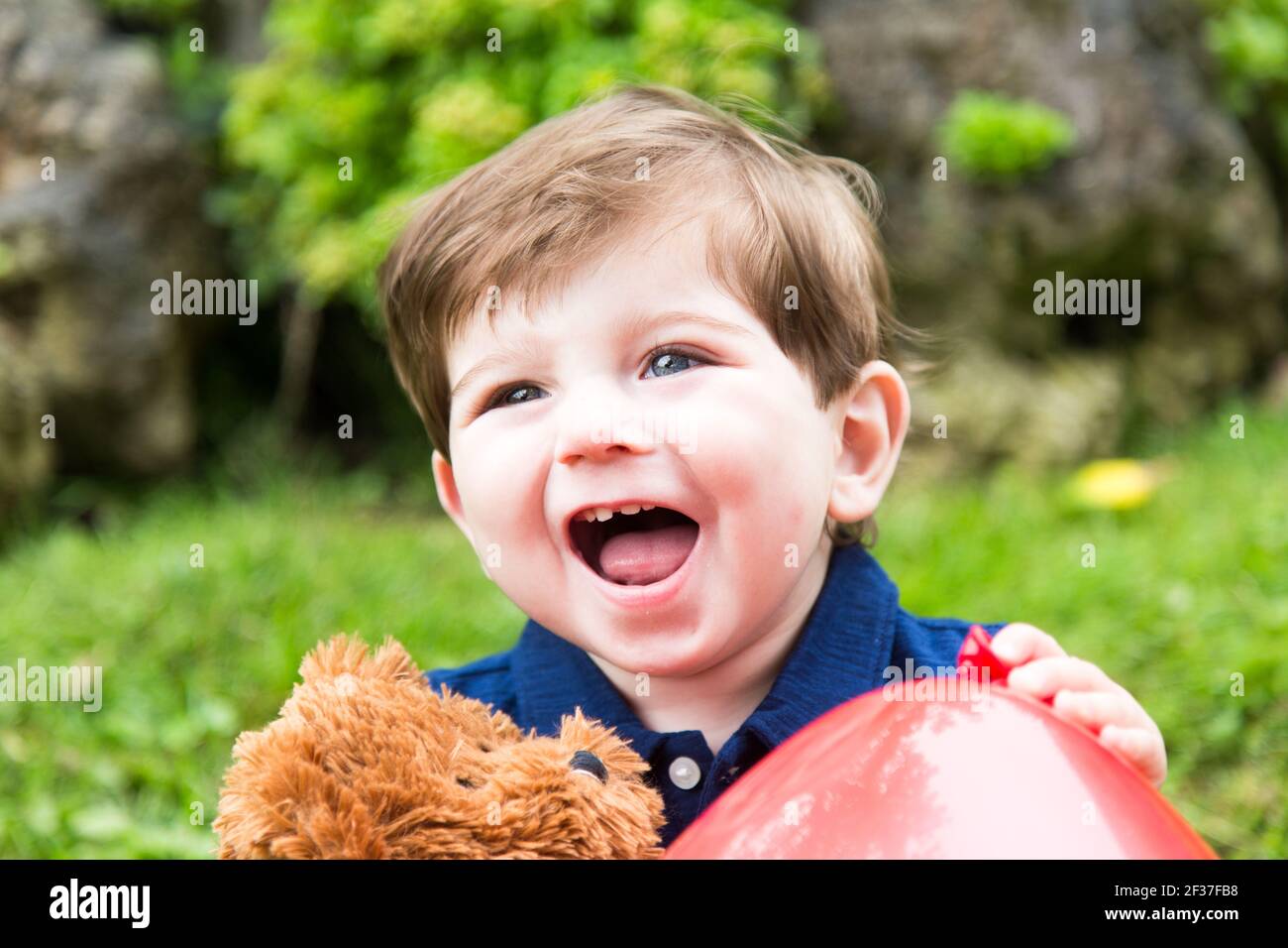 petit garçon jouant avec un ours en peluche et un rouge montgolfière dans le jardin Banque D'Images