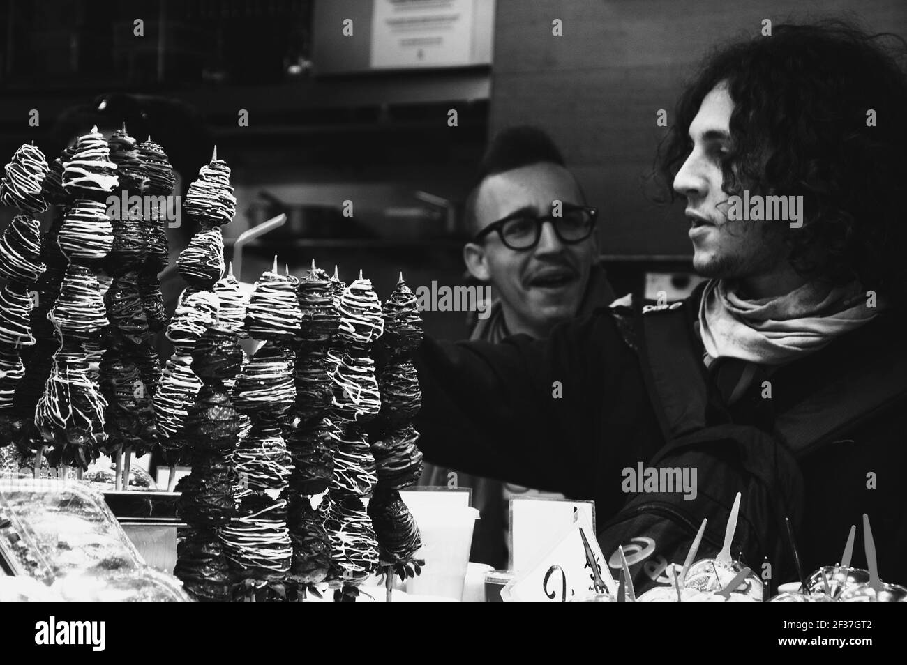 Les jeunes hommes achètent des brochettes de fraises fraîches enrobées de chocolat de la boîte aux fruits du célèbre marché alimentaire de Barcelone la Boqueria. Barcelone, Espagne. Noir blanc Banque D'Images