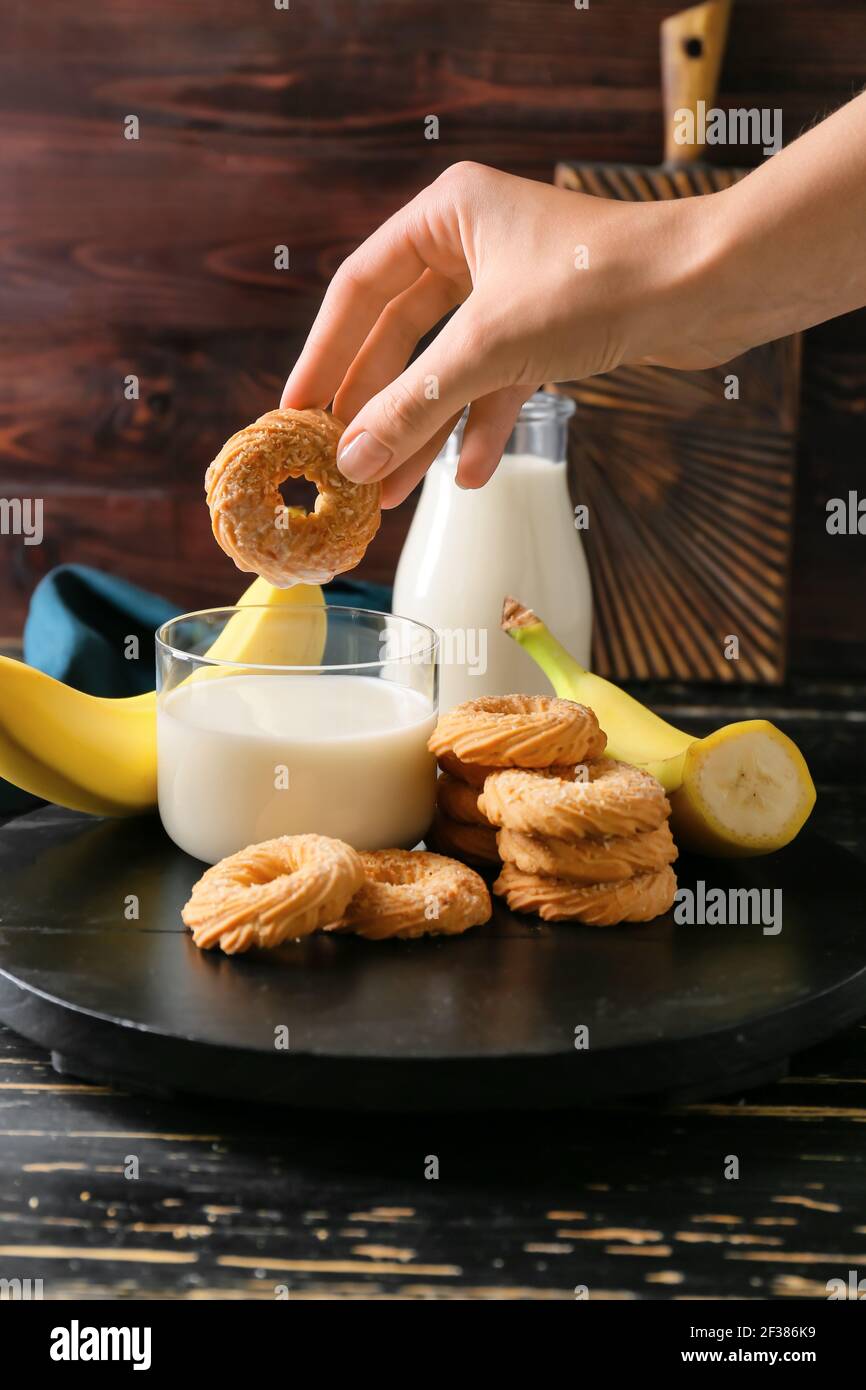 Main femelle avec un délicieux biscuit à la banane et du lait sur le noir arrière-plan en bois Banque D'Images
