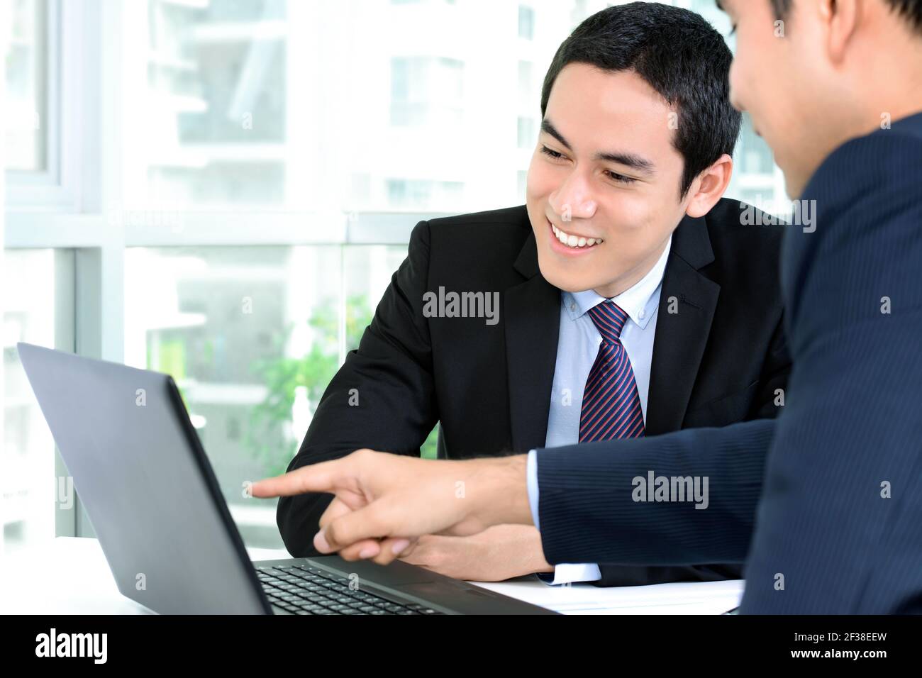 Des hommes d'affaires asiatiques souriants discutent et regardent un ordinateur portable la réunion Banque D'Images