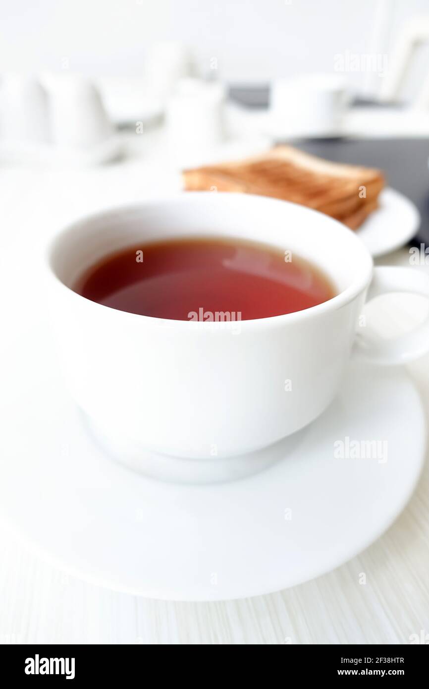 Thé chaud dans une tasse blanche avec des toasts flous sur la table comme arrière-plan, concept petit déjeuner - flou artistique Banque D'Images