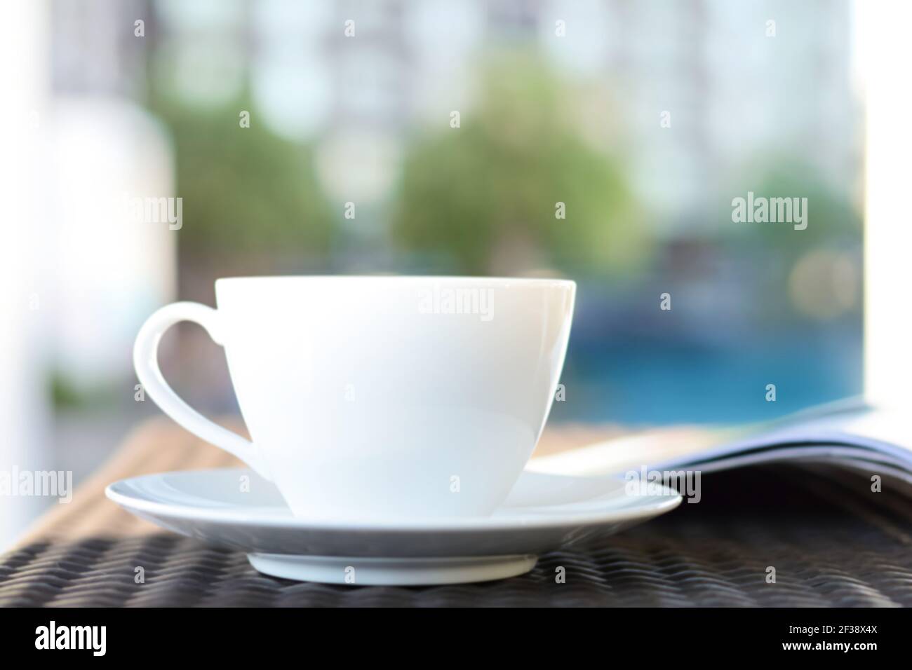 Tasse à café floue avec livre ouvert sur une table extérieure en rotin le matin - se détendre dans la station ou à l'hôtel concept Banque D'Images