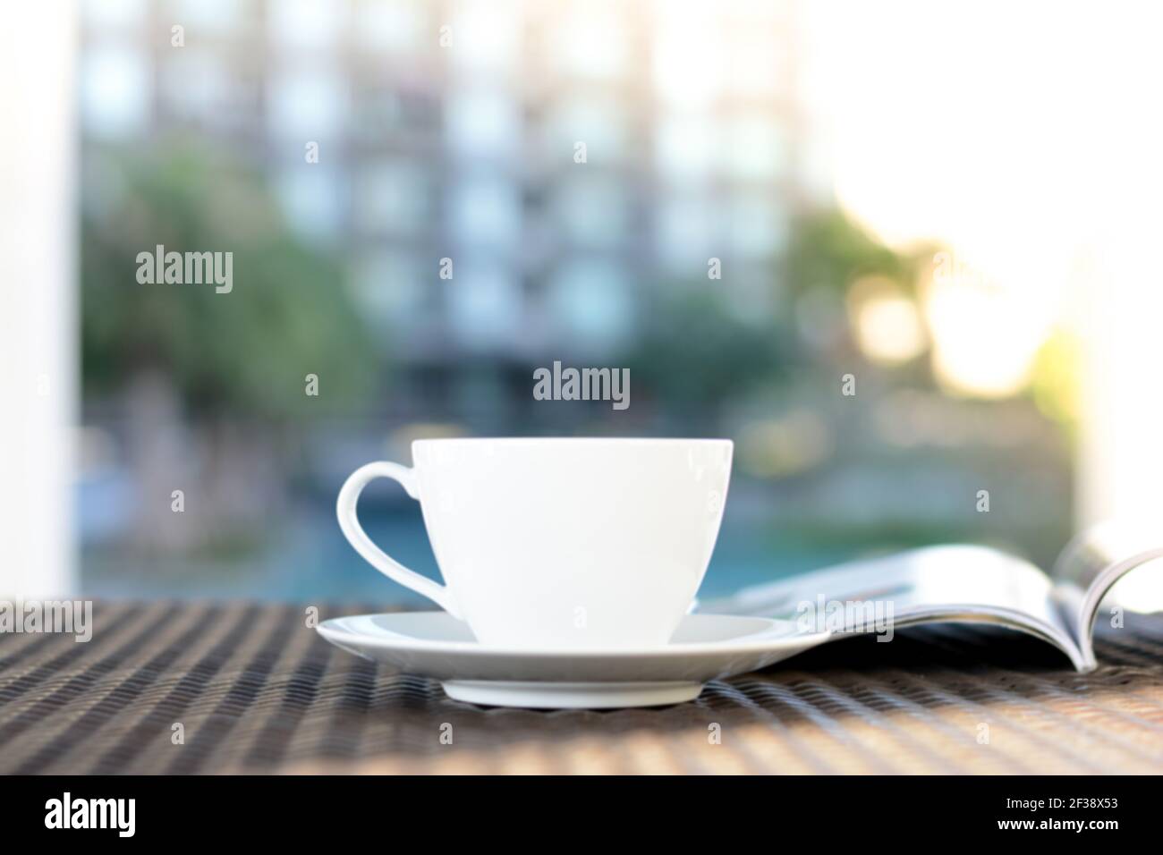 Tasse à café floue avec livre ouvert sur une table extérieure en rotin le matin - se détendre dans la station ou à l'hôtel concept Banque D'Images