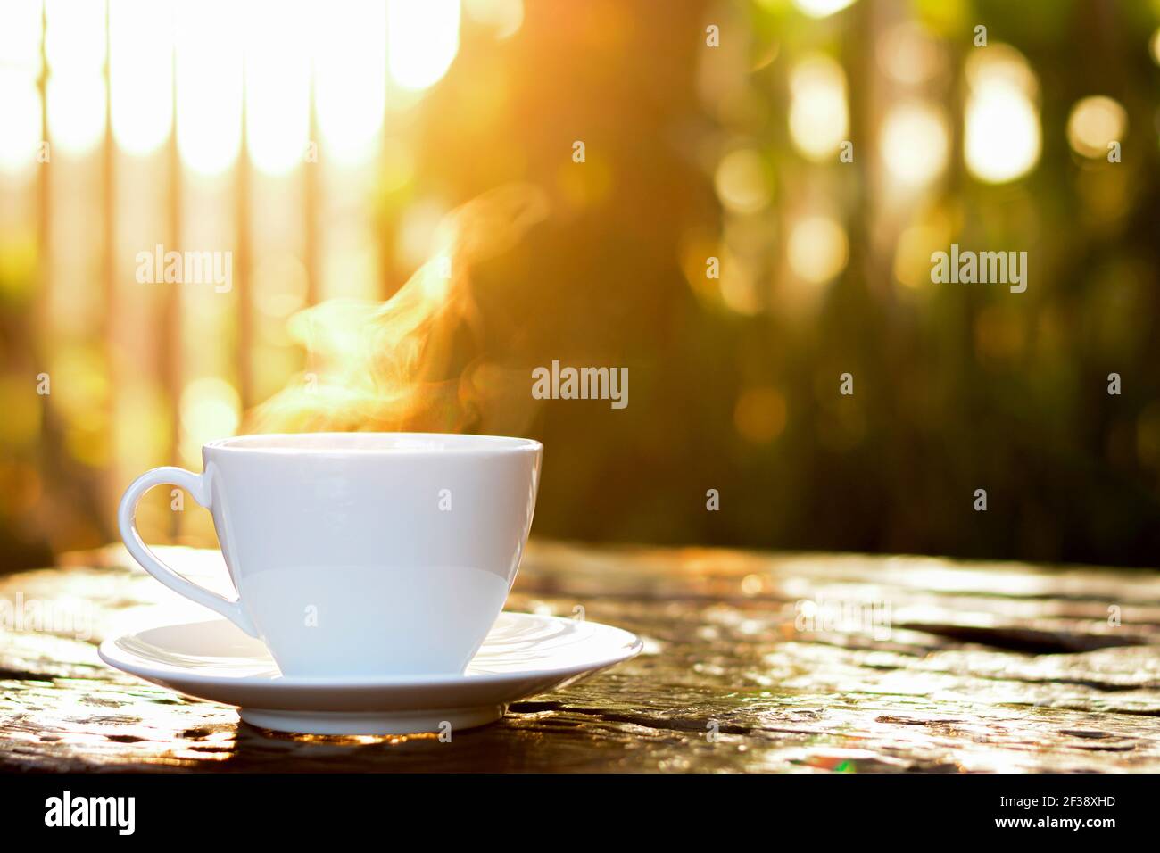 Une tasse de café avec du café chaud sur une ancienne table en bois lumière du soleil et arrière-plan vert nature flou Banque D'Images