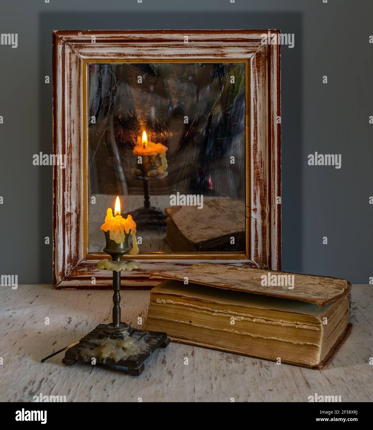 Une bougie allumée se reflète dans un vieux miroir dans un cadre en bois et illumine les livres sur la table. Vintage. Banque D'Images
