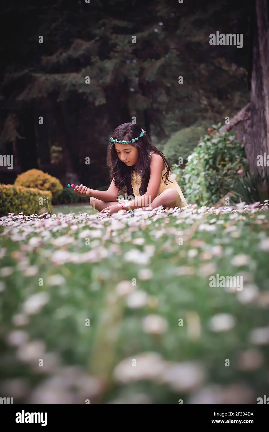 Adolescente assise sur l'herbe dans un parc portant une robe hippie jaune et une couronne de fleurs Banque D'Images