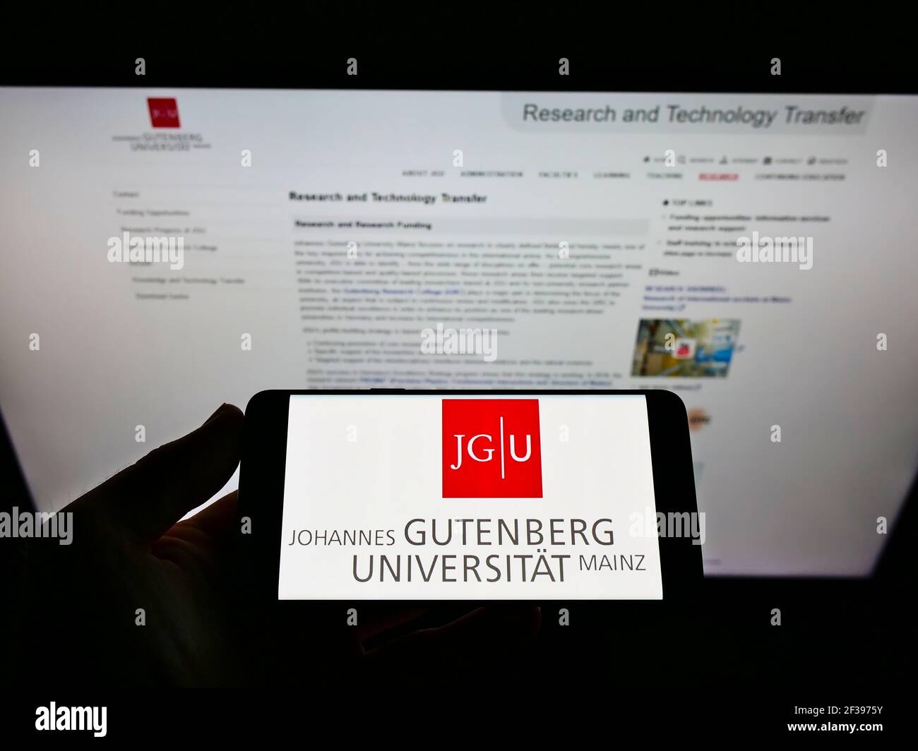 Personne tenant un smartphone avec le logo de l'université allemande Johannes Gutenberg-Universität Mainz à l'écran devant le site. Mise au point sur l'affichage du téléphone. Banque D'Images