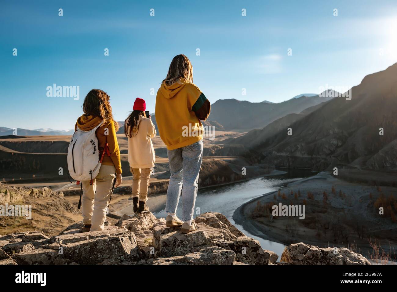 Trois femmes touristes ou randonneurs sont debout sur la falaise et vue sur la rivière et les montagnes au coucher du soleil Banque D'Images