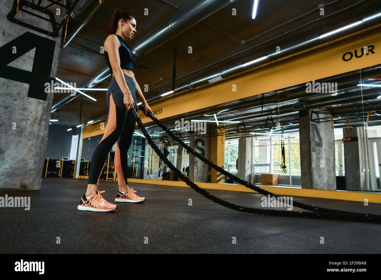 Entraînement de force. Jeune femme sportive forte s'exerçant avec des cordes de combat à la salle de sport crossfit, pleine longueur Banque D'Images