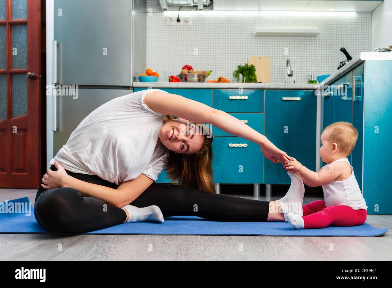 Une Jeune Mere Et Son Bebe S Etirent Sur Un Tapis Dans La Cuisine L Enfant S Assoit Pres De La Jambe De La Mere Le Concept De L Entrainement Sportif A Domicile Avec Chi Photo
