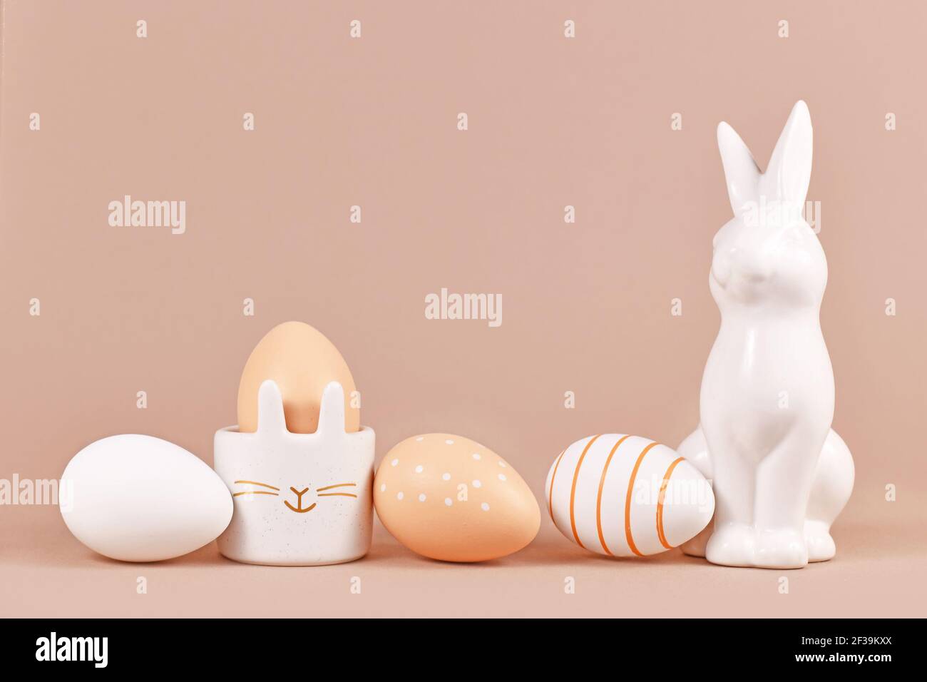 Œufs de Pâques de couleur naturelle avec rayures simples et motif à pois avec coquetier en forme de lapin et sculpture beige fond avec espace de copie vide Banque D'Images