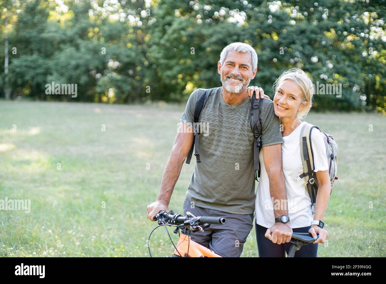 Portrait d'un couple mûr souriant avec vélo debout en forêt Banque D'Images