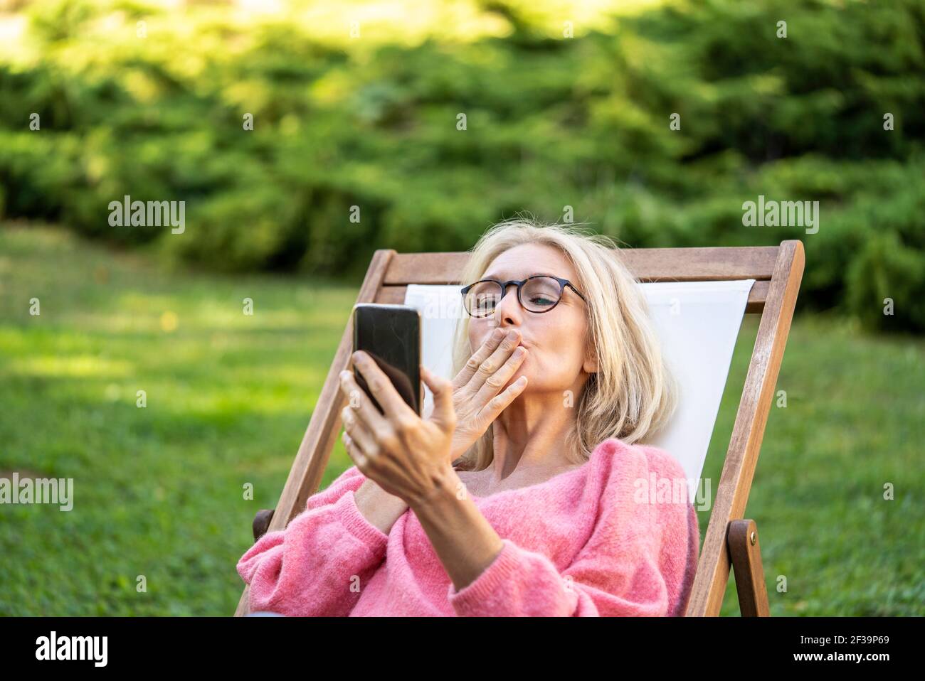 Une femme mûre souriante s'embrasse tout en visiophant un téléphone intelligent Banque D'Images