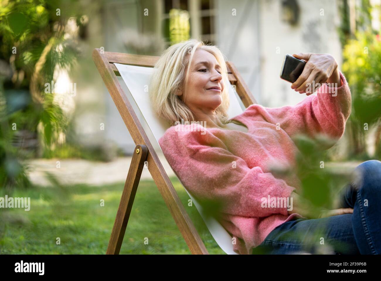 Femme mûre souriante utilisant un smartphone tout en étant assise sur un transat Banque D'Images