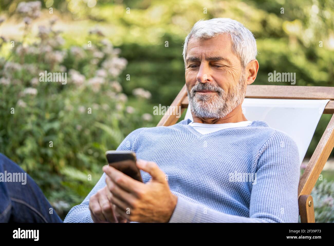 Homme mûr souriant utilisant un smartphone tout en étant assis sur un transat Banque D'Images