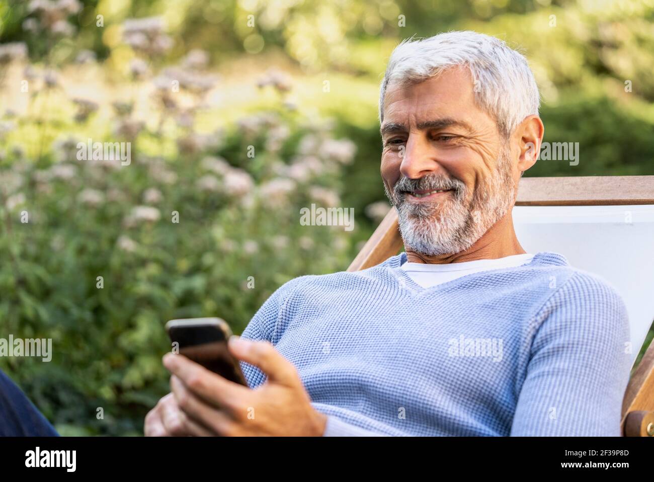 Homme mûr souriant utilisant un smartphone tout en étant assis sur un transat Banque D'Images