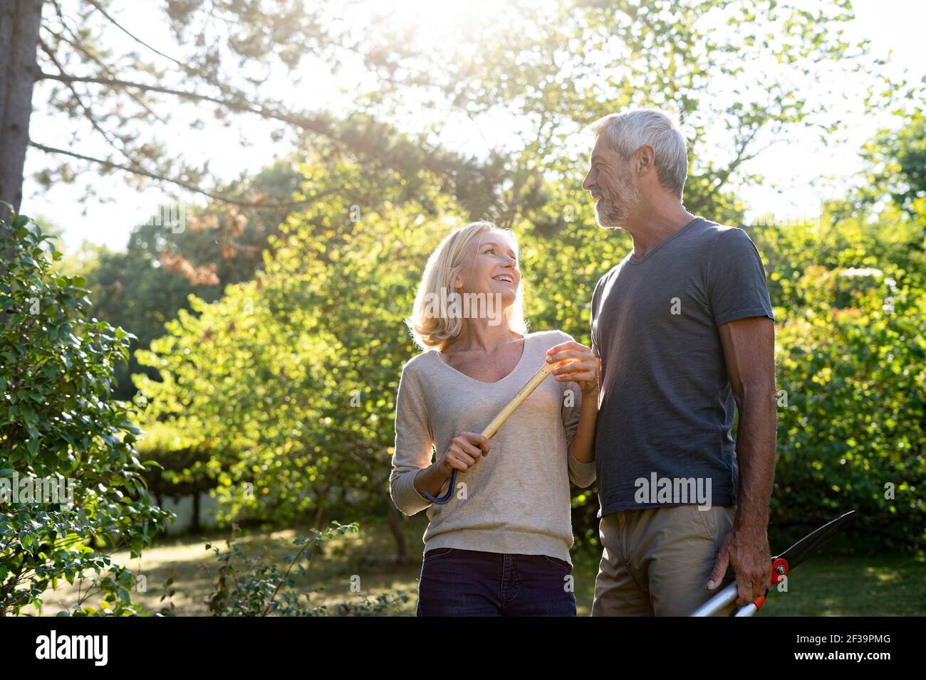 Couple mûr souriant avec équipement de jardinage debout dans l'arrière-cour Banque D'Images